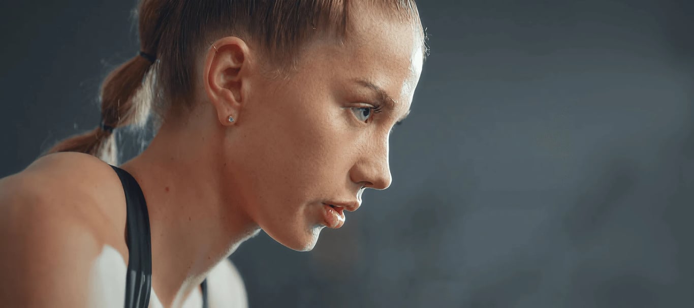 full-bleed dark photo of a focused woman in profile with a blonde ponytail and black sports top, mid-workout