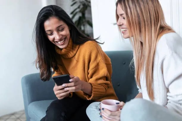 Two friends on a sofa sharing a referral code on a phone