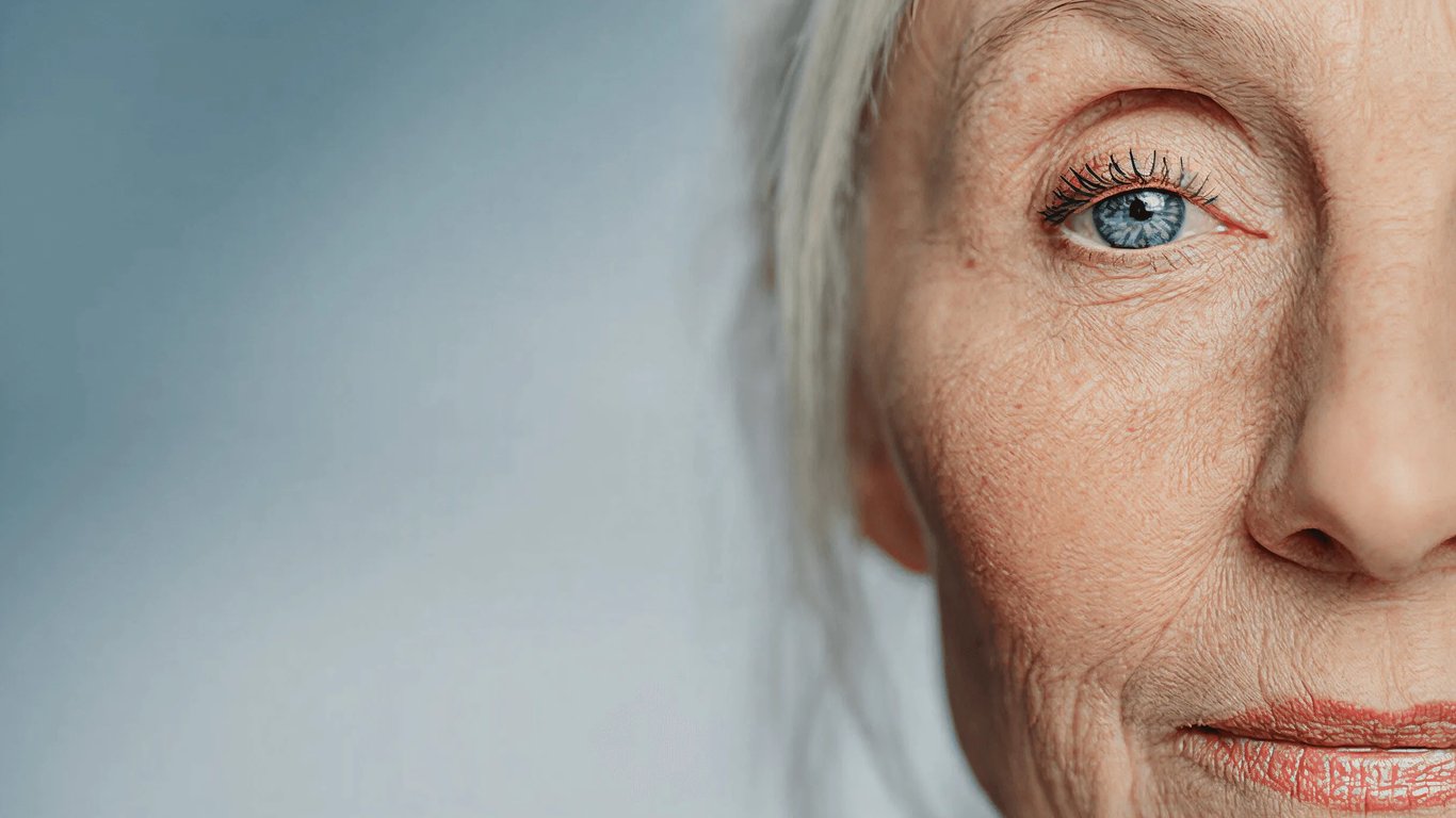 close-up of an older woman's blue eye and weathered skin against a blue-grey backdrop