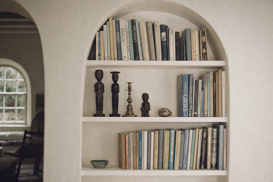 White plaster bookshelves built into a curved wall, filled with vintage books and small sculptural objects.
