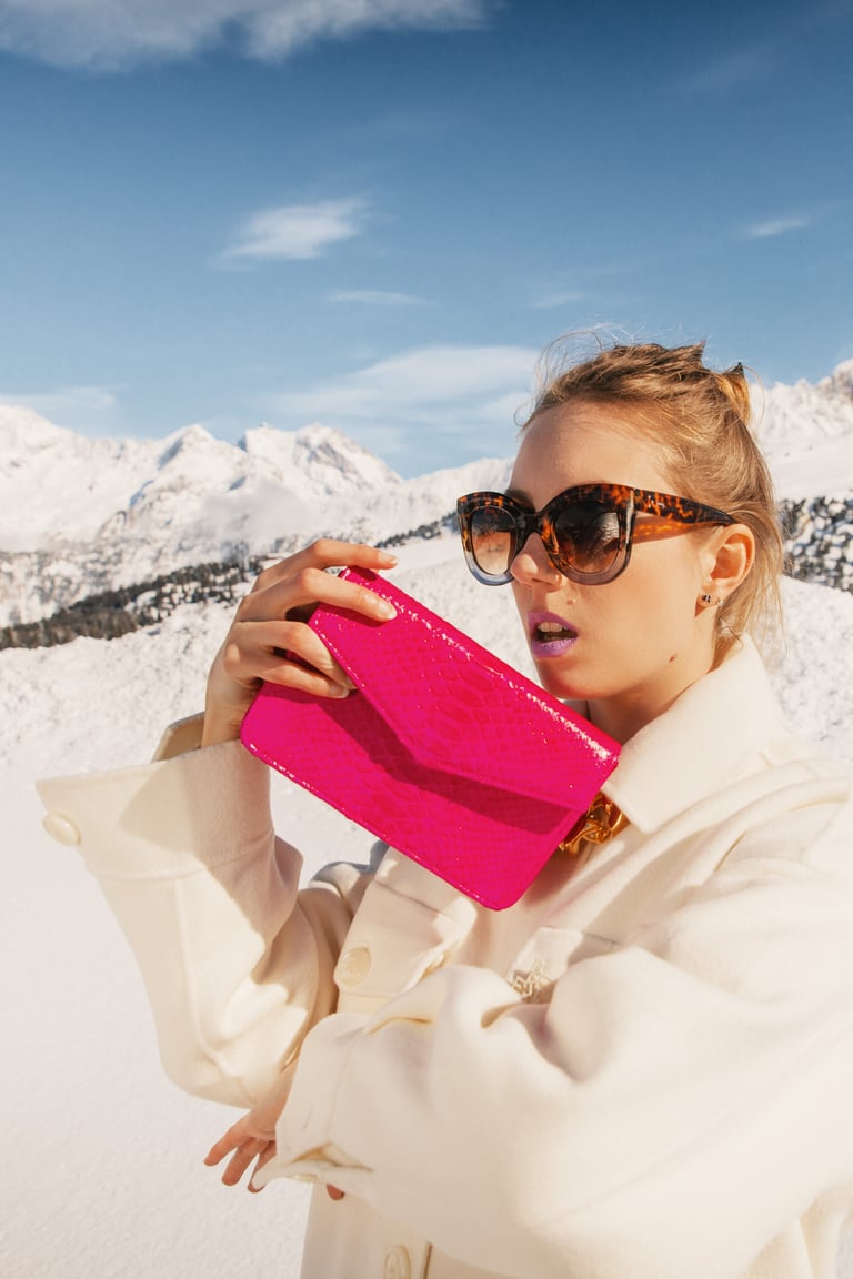 Blonde woman taking a selfie in the snow with a pink bag