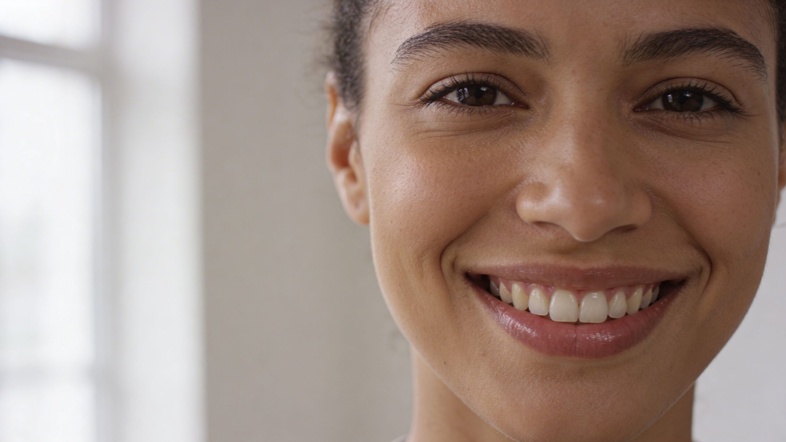 A close-up headshot of a smiling woman with clear skin, showcasing a friendly and approachable expression.