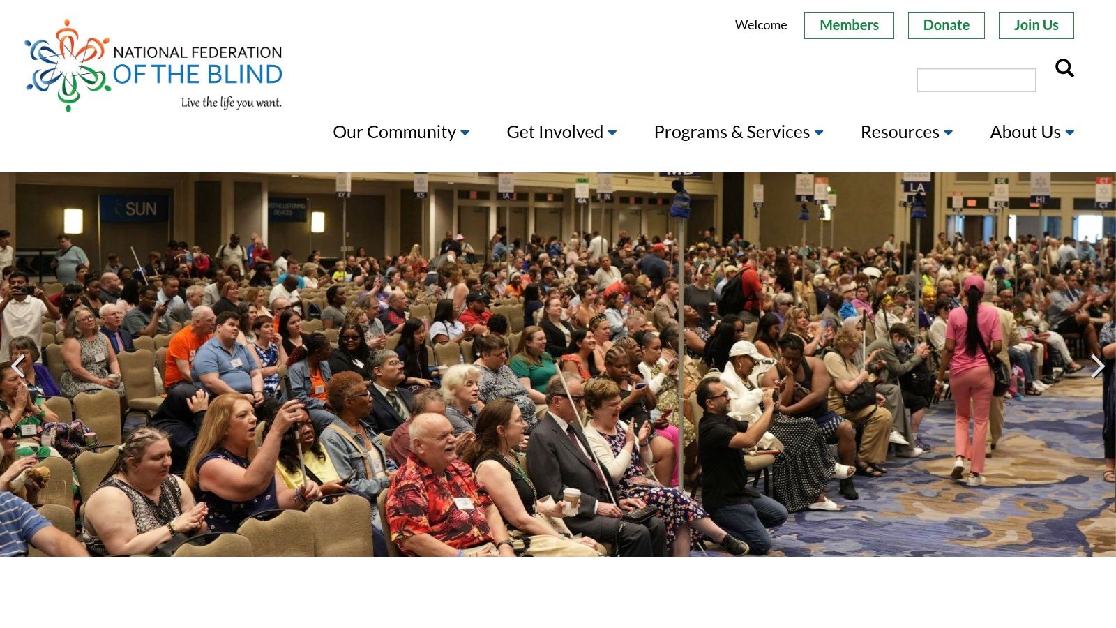 A group of people, some using white canes, gather and talk at what appears to be a conference or large meeting, representing the community aspect of the National Federation of the Blind.