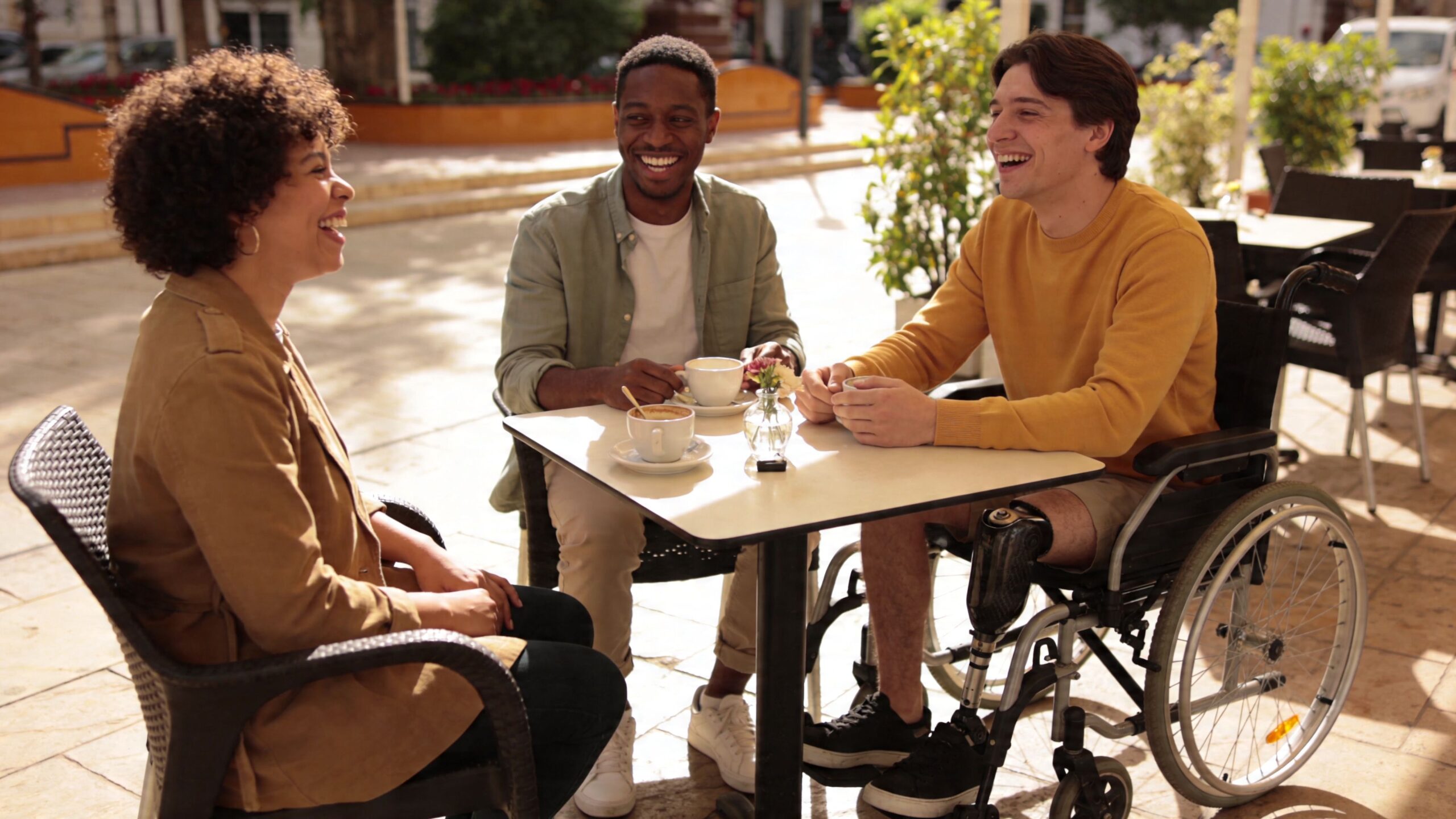 A diverse group of friends smiling and laughing while enjoying coffee together at an outdoor cafe table.