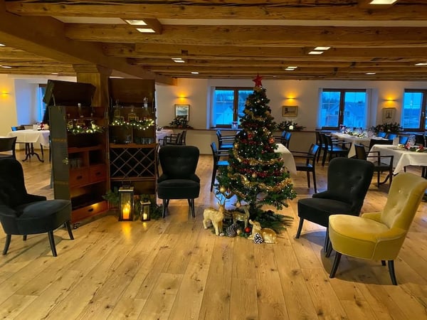 Decorated Christmas tree in the Löwen Hall with comfortable velvet armchairs. Rustic wooden beam ceiling and warm lighting.
