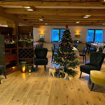 Decorated Christmas tree in the Löwen Hall with comfortable velvet armchairs. Rustic wooden beam ceiling and warm lighting.