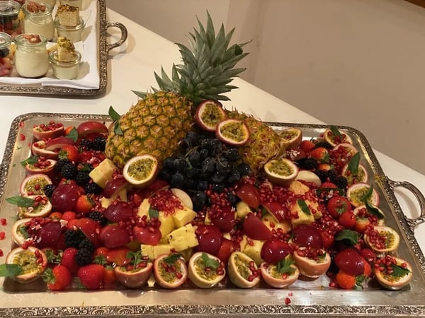 Opulent fruit platter on silver tray with pineapple, passion fruits, pomegranate and dark grapes. Decoratively arranged with berries.