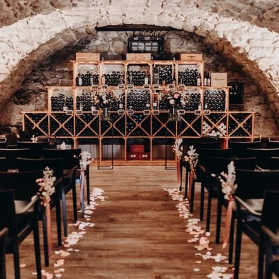 Romantische Trauungslocation mit Blick auf die Weinregale. Stuhlreihen mit Blumengestecken und Rosenblättern dekoriert.