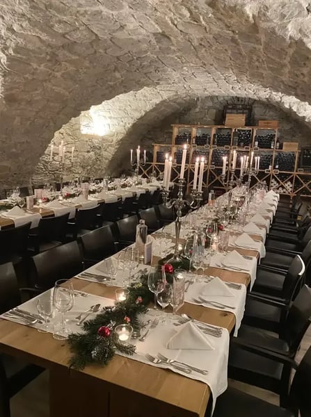 Christmas banquet table in wine cellar with evergreen decorations and candelabras. Atmospheric lighting enhances the ambiance.