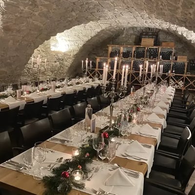 Christmas banquet table in wine cellar with evergreen decorations and candelabras. Atmospheric lighting enhances the ambiance.