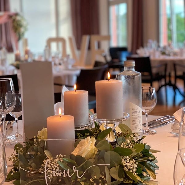 Elegant table centerpiece featuring grey candles, surrounded by eucalyptus leaves, white roses and baby 's breath. Handwritten table number.