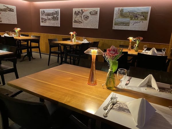 Evening mood in a cozy Swiss 'Stübli' with historic postcards on brown walls, wooden tables illuminated by amber lamps, and decorated with fresh pink flowers.