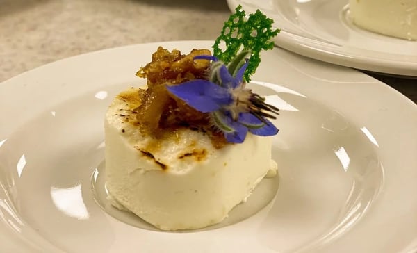 Goat cheese amuse-bouche with caramelized crust, garnished with edible borage flower and fresh herbs.