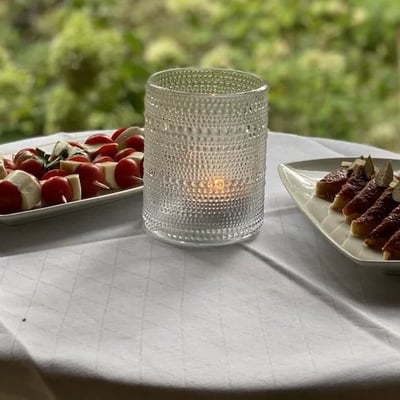 Elegant appetizers on white tablecloth: caprese skewers and aged ham, decoratively presented with tealight.