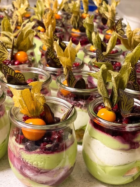Festive dessert glasses with pistachio cream, berries and physalis, decorated with chocolate garnish and dried fruit.