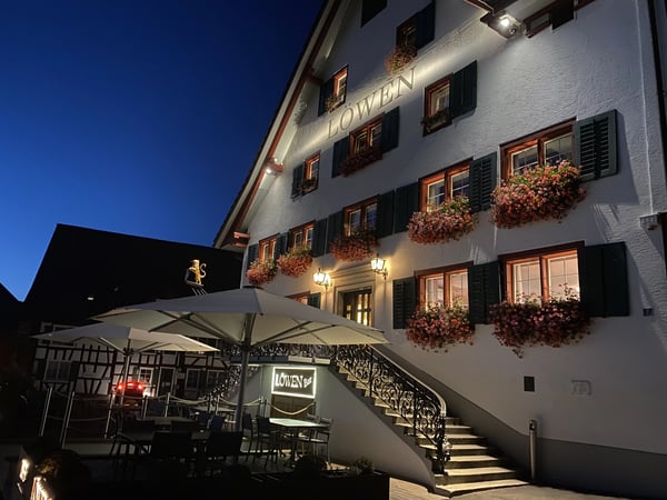Evening view of Restaurant Löwen, a traditional white Swiss building with illuminated facade.