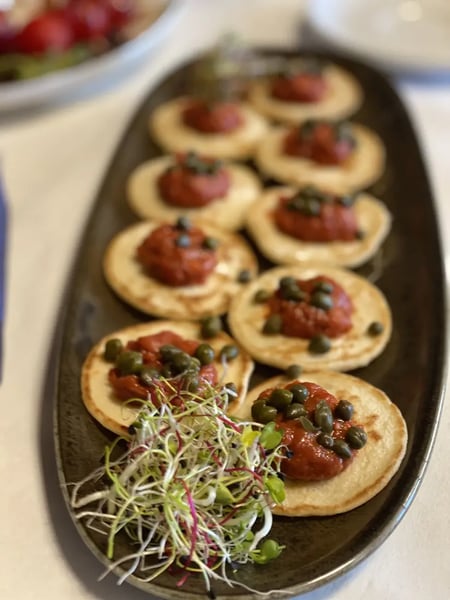 Mini blinis topped with tuna tartare, capers and fresh sprouts as elegant appetizer.