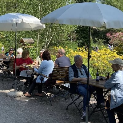Cozy garden restaurant with wooden benches and sun umbrellas. Guests enjoying refreshments amid flowering moorland.