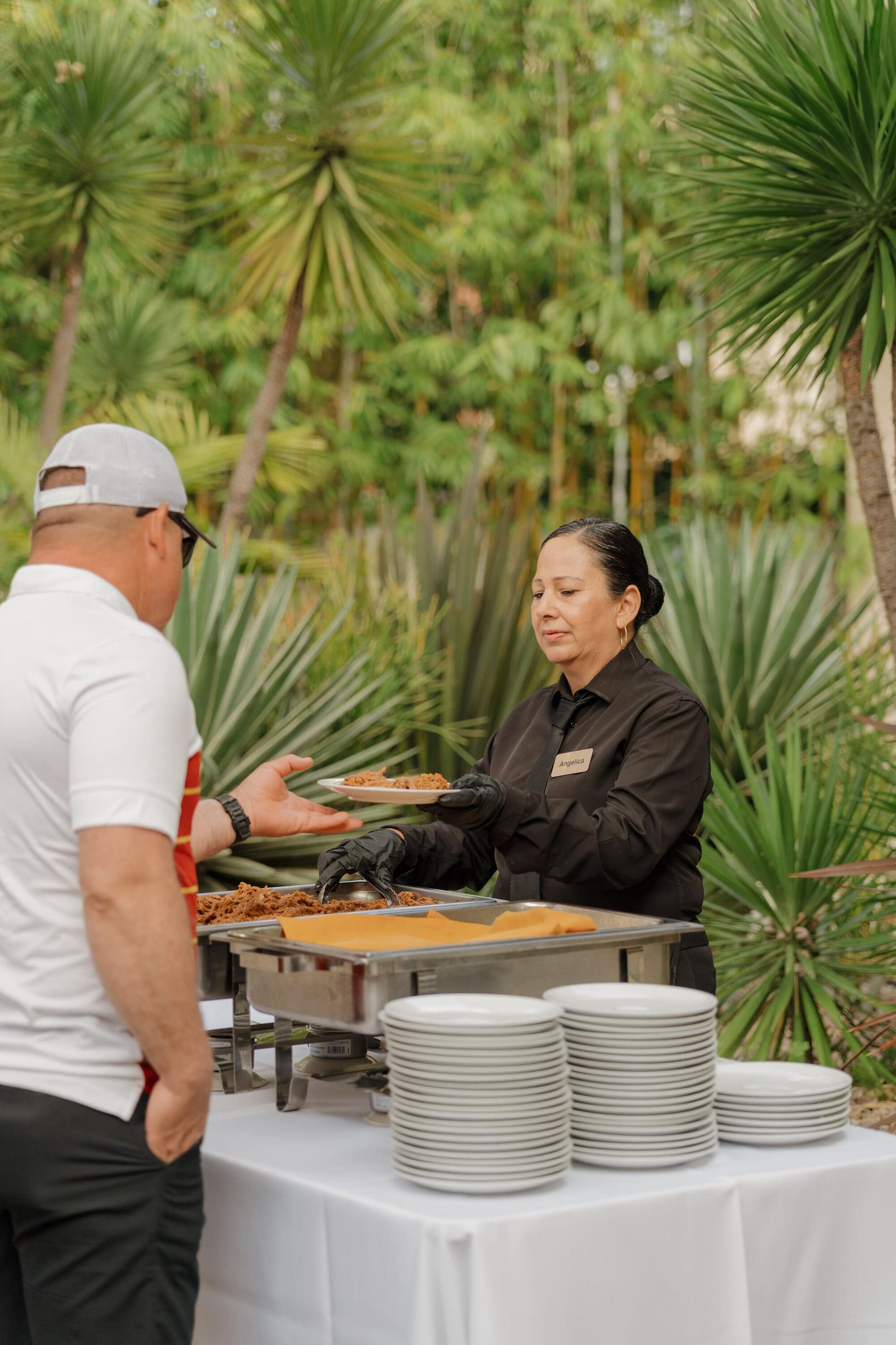 Outdoor buffet service with a staff member plating for a guest among palms.