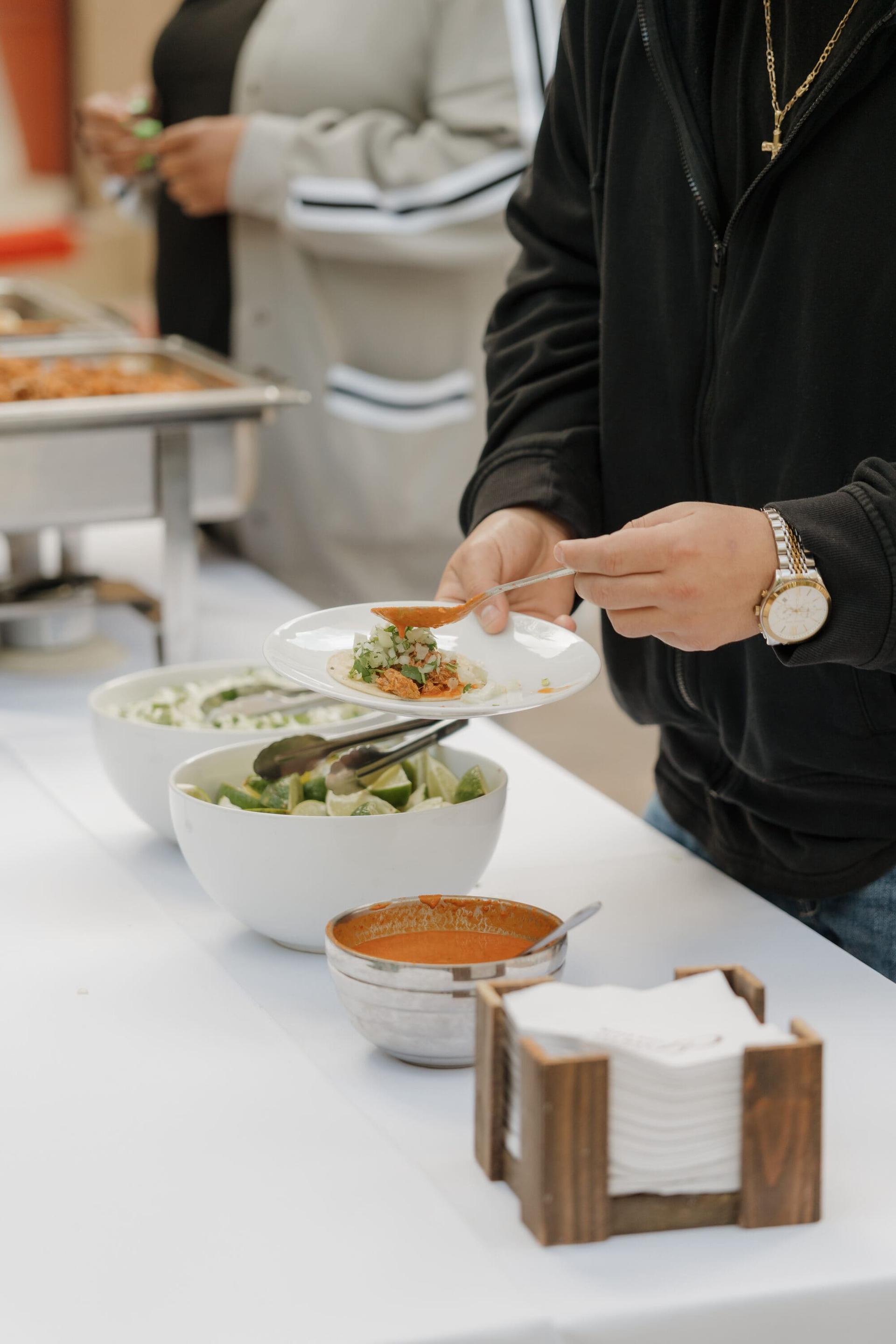 Guest serving a plate at the buffet with fresh sides and salsa.