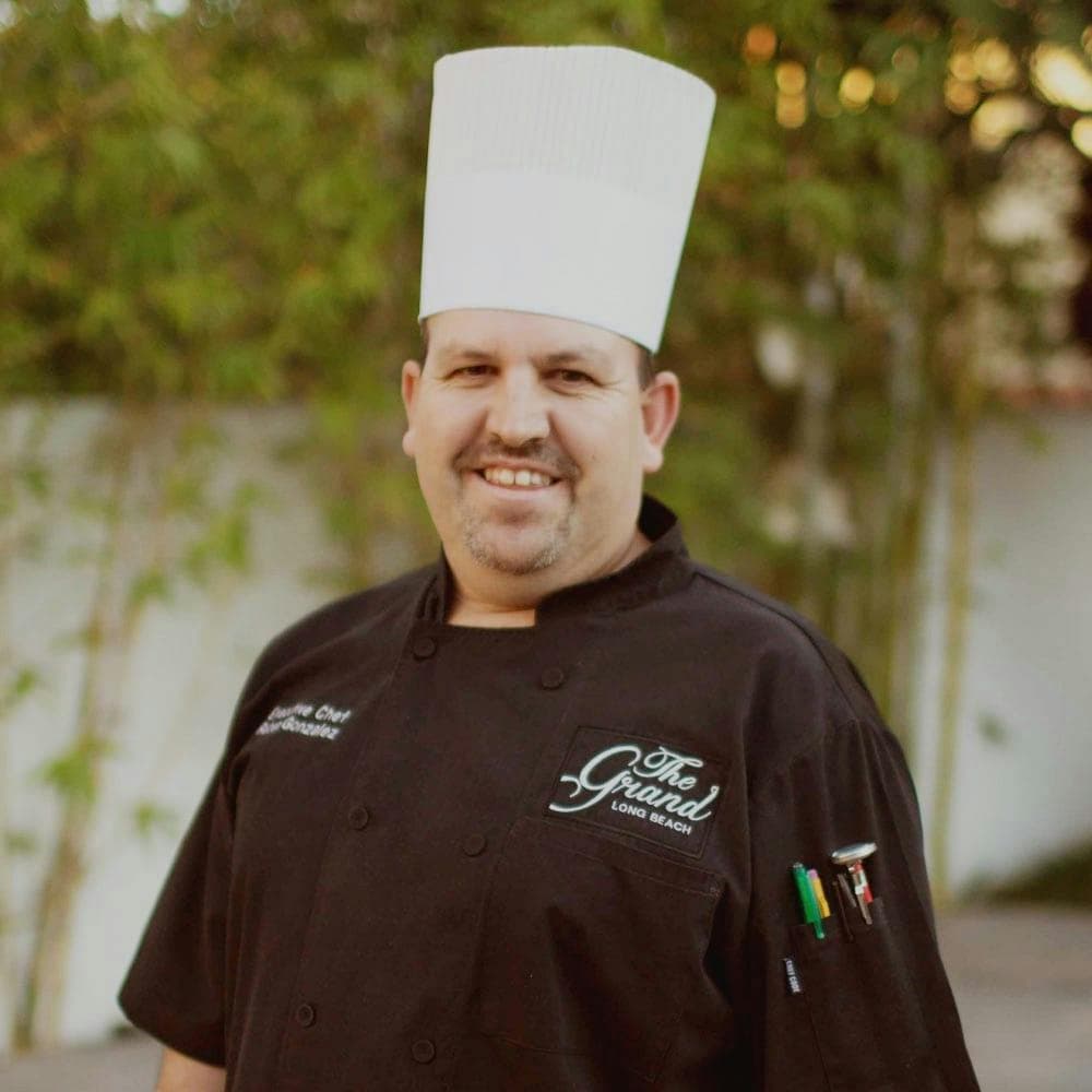 Chef in whites arms crossed in commercial kitchen.
