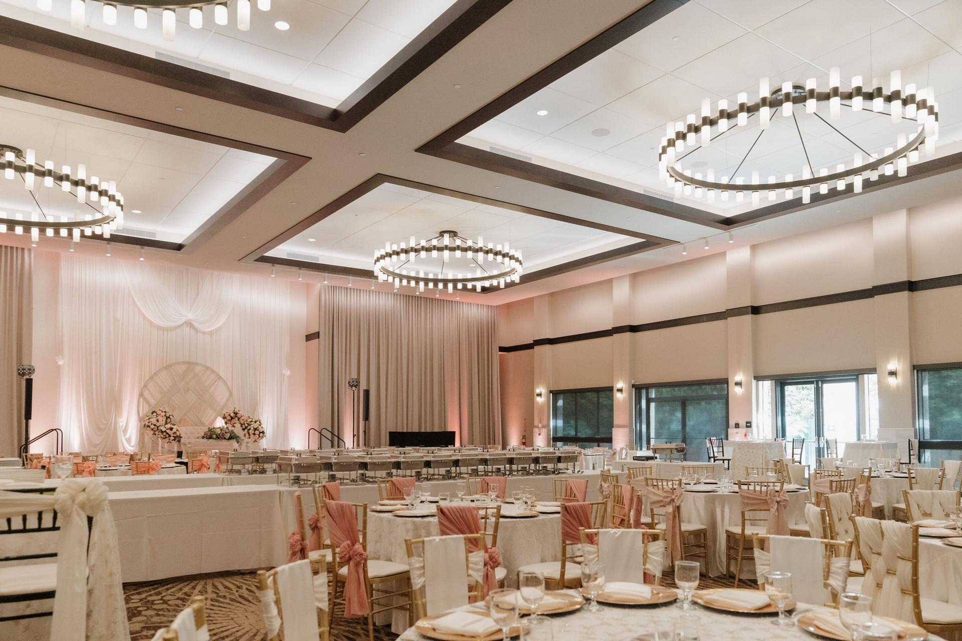 Grand Ballroom social setup with round tables, blush chair sashes, and pink uplighting.