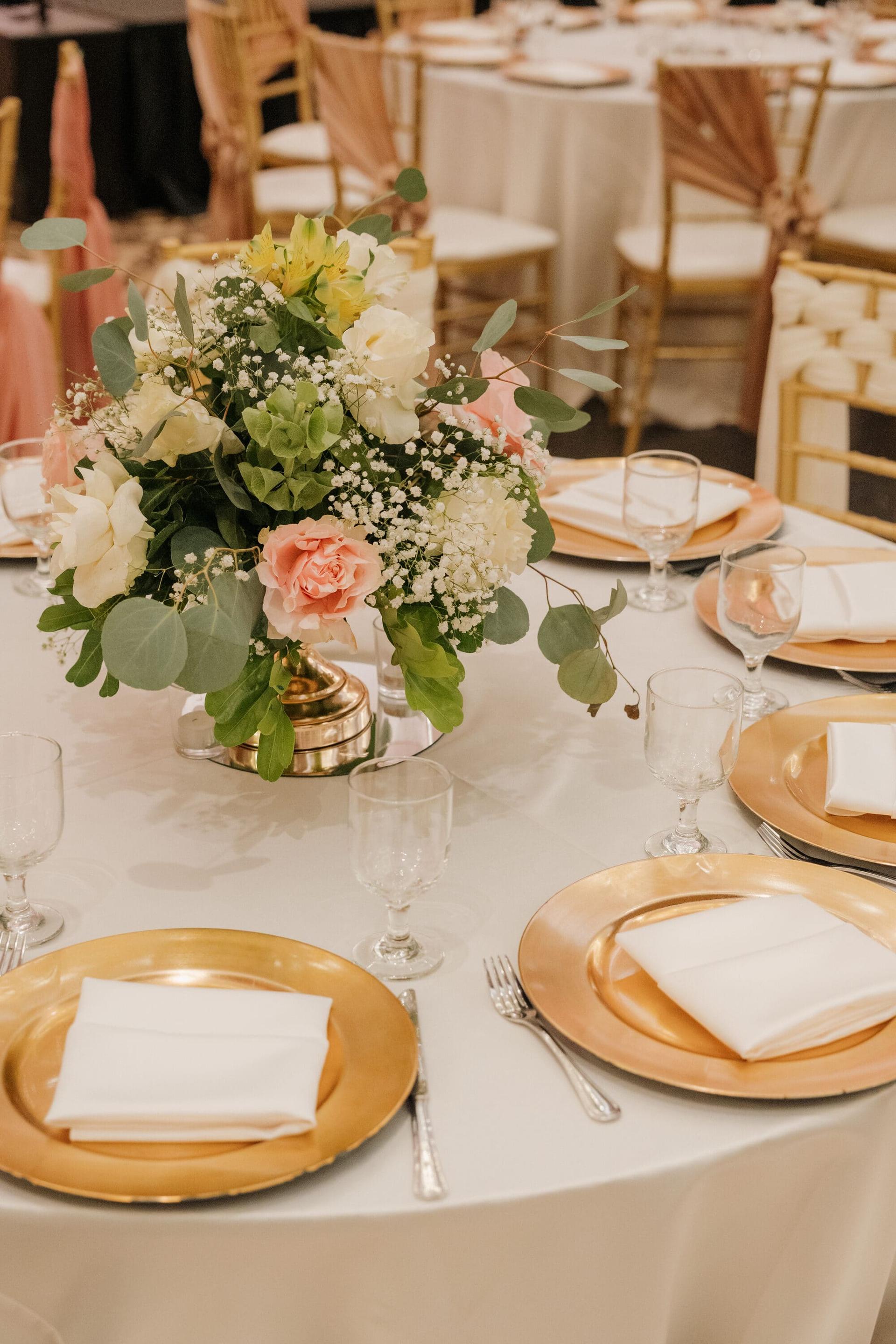 Place setting with gold chargers and a floral centerpiece in the Grand Ballroom.