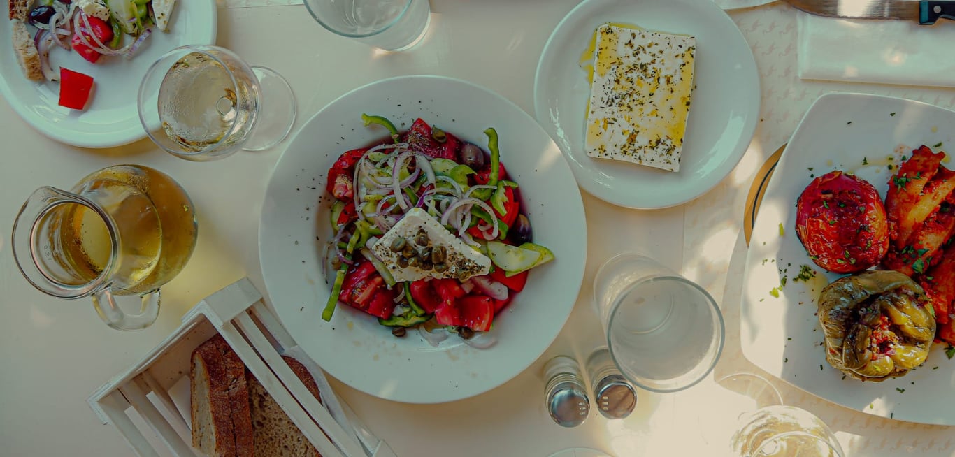 Picture of a table full of Traditional Greek delicacies. A Greek salad (choriatiki), Feta cheese, Gemista (stuffed tomatoes, peppers and eggplants) and local white wine.