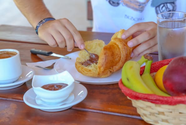 Image of a person eating breakfast consisting of a croissant and coffee