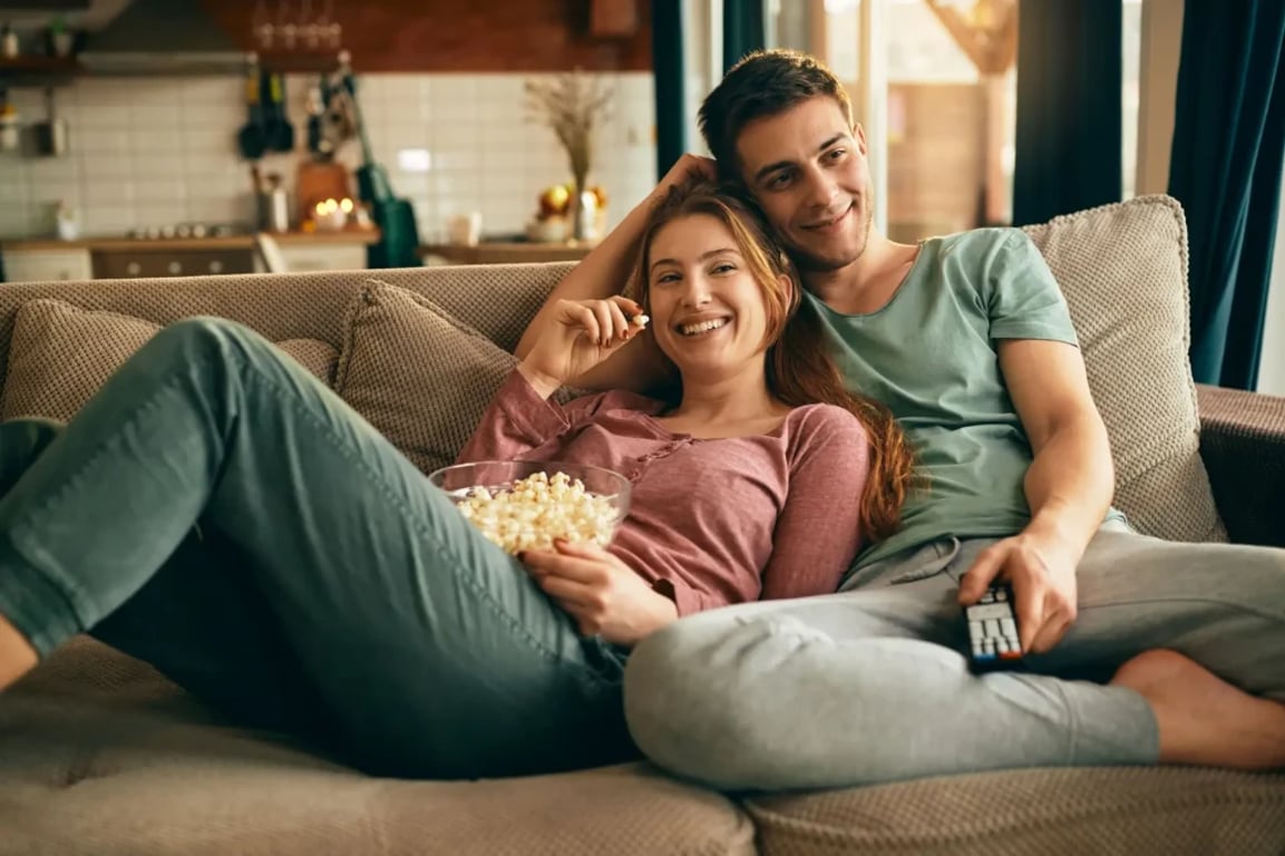 pár se dívá doma na gauči na film, dopřává si misku plnou popcornu