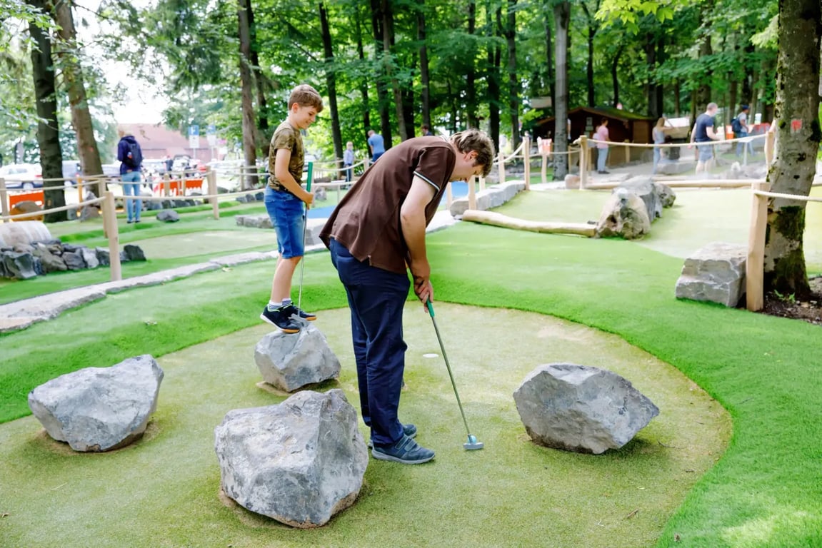 Otec a syn spolu hrají minigolf. Oba vypadají šťastně. Je krásný den, protože na sobě mají spíše letní oblečení.