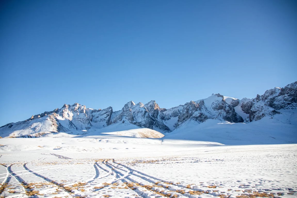 Zasněžená krajina, kde lze pozorovat hory a jasnou oblohu.