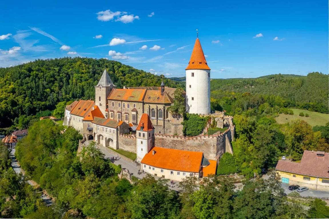 Letecký pohled na hrad Křivoklát a jeho okolí. Vidět jdou lesy v dáli a modrá obloha.