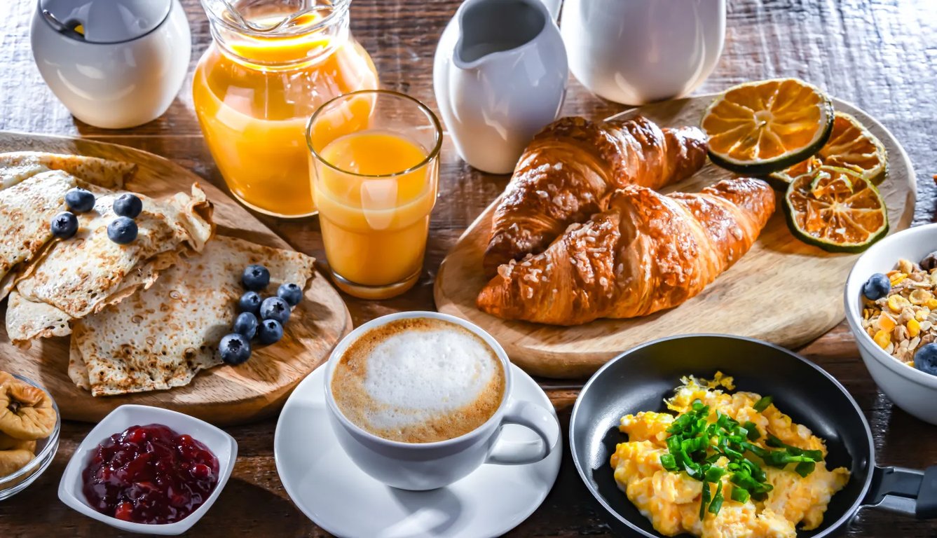 Bohatý snídaňový stůl s kávou, džusem, vajíčky, croissantem, palačinkami a dalších lahodných pokrmů.