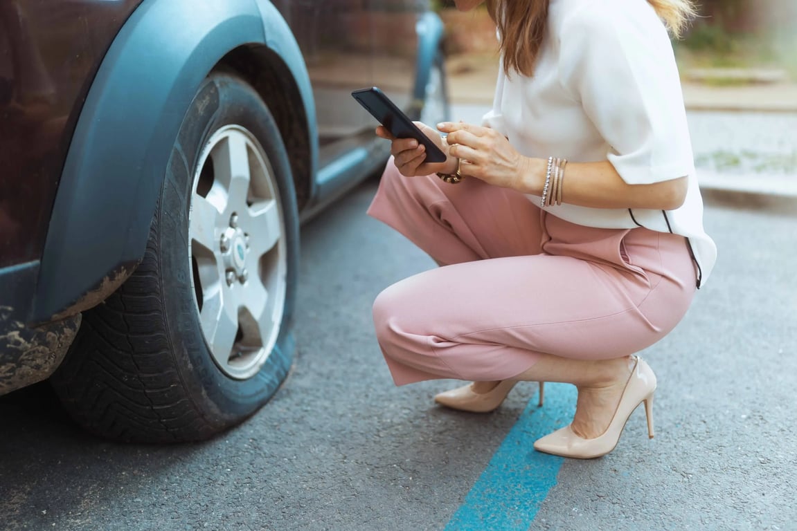 Žena dřepí u prasklé pneumatiky