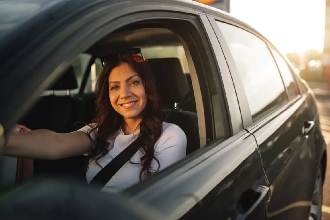 Žena sedí v autě a usmívá se, zatímco drží volant