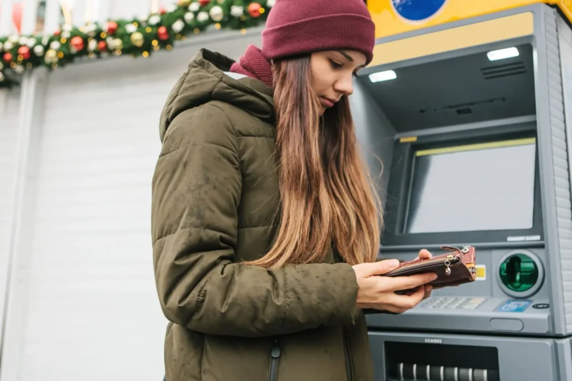 Žena stojí před bankomatem a dívá se do peněženky