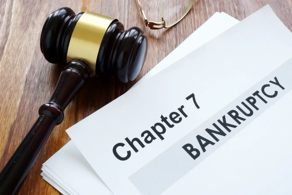 Na hnědém stole leží kladívko soudce a papíry. Na vrchním papíře je napsané „Chapter 7 BANKRUPTCY