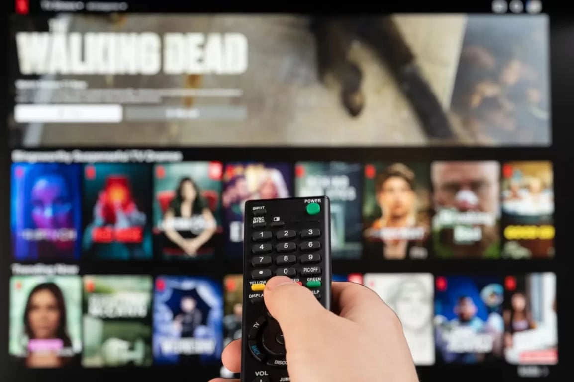 Ruka s ovladačem ukazuje na TV s výběrem filmů