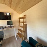 Small room with white shiplap walls and a natural wood plank ceiling, with a desk and a shelf.