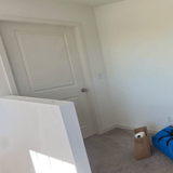 Empty upstairs room with a white paneled door, textured walls and carpet.
