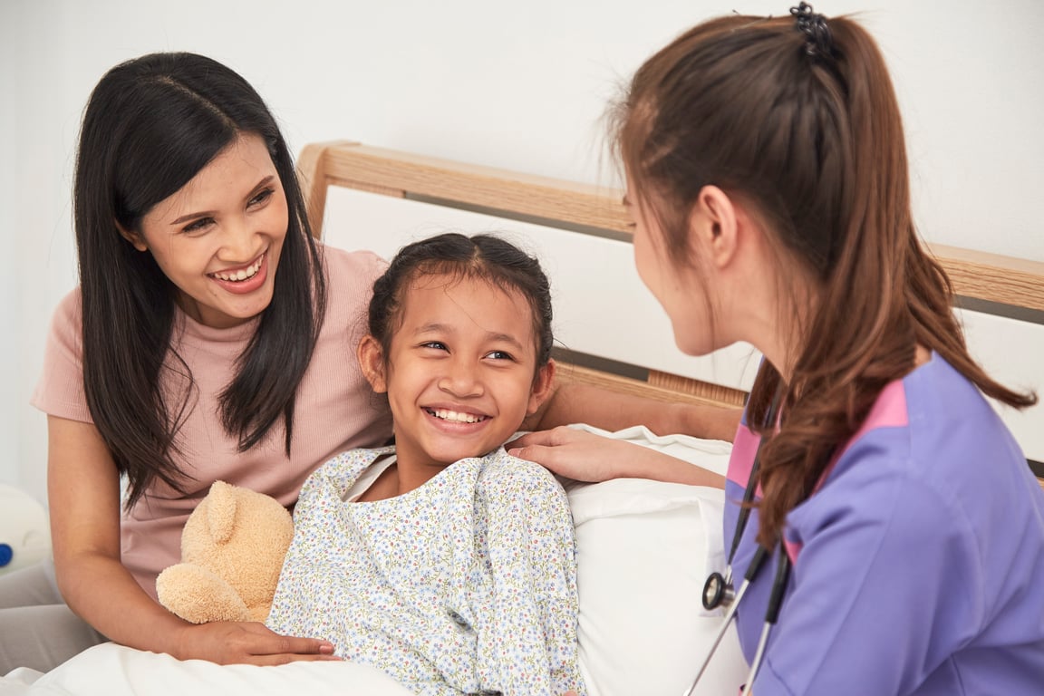 Smiling nurse and young girl in a hospital bed.