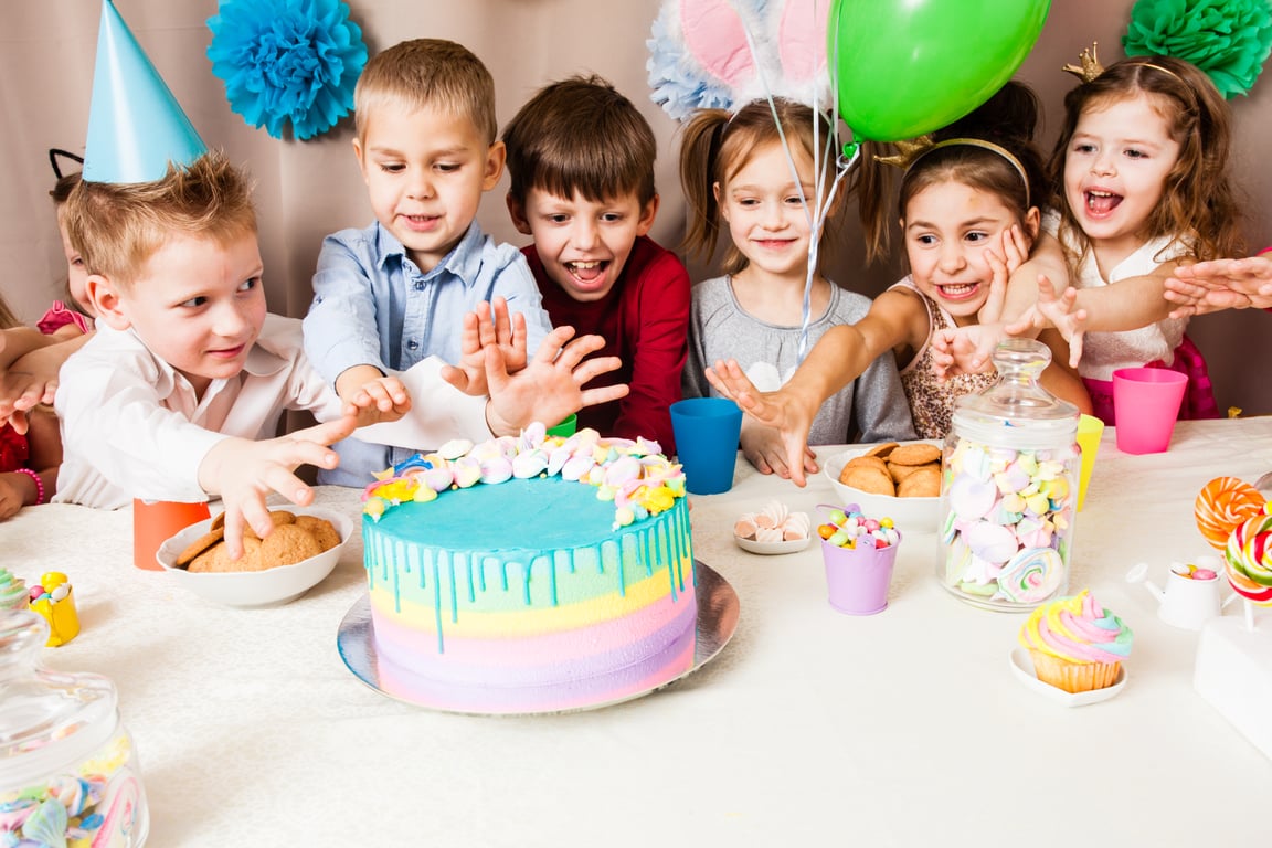 Children cheerfully reaching for cake.