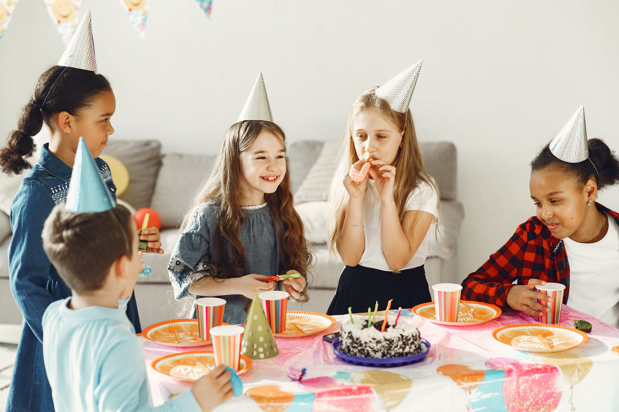 Children wearing party hats gathered around a birthday cake at a kids birthday party at home.