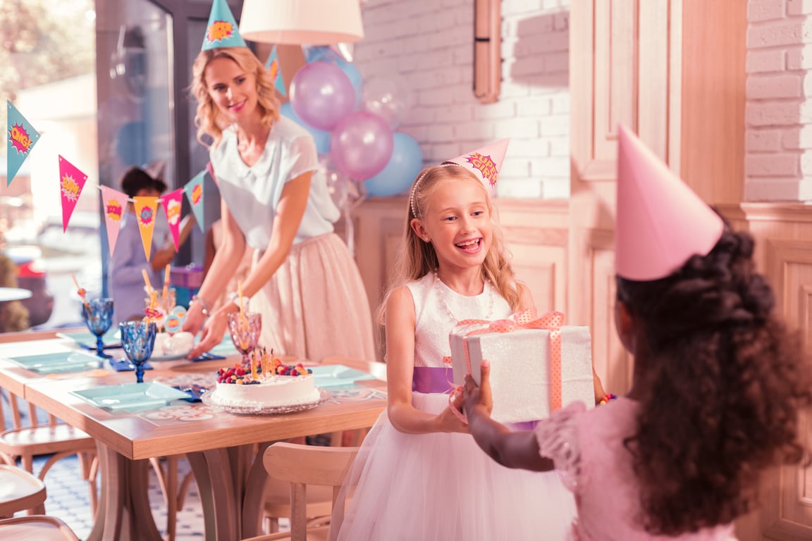 Child in a princess dress smiling at a birthday party with balloons and decorations.