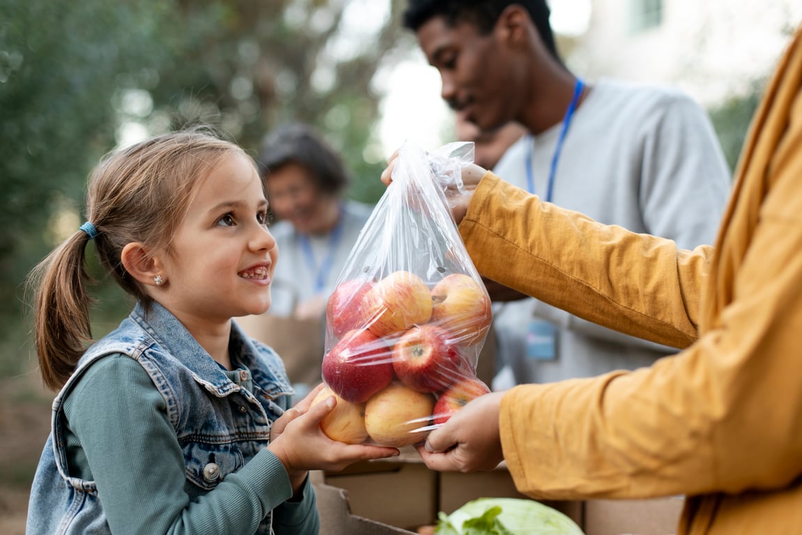 Child smiling while helping pack food donations with Second Harvest volunteers.