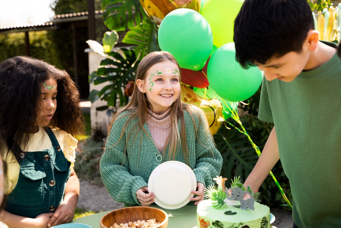Children having fun at a jungle themed birthday party, there is a green cake with a figure elephant on top.