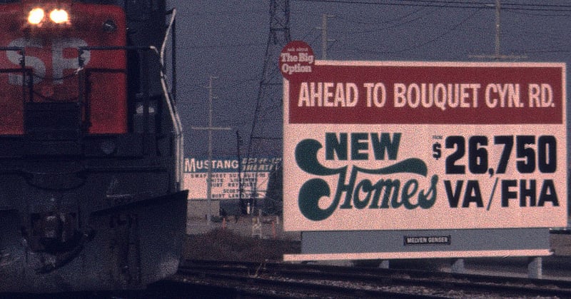 This is a detail of a photo of a train but the marquee for the Mustang Drive-in was in the background I am not sure of the year but by the home price billboard I would say in the 70's maybe.
