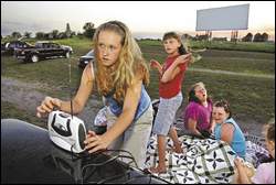 The sun sets behind the big screen at Sunshine Mine Drive-In, west of Centerville, as Hannah Hillyard, 12, adjusts a radio to receive the sound for the movie that’s about to start. Behind her, from left, are her sisters Heidi, 9, and Haley, 11, and cousin