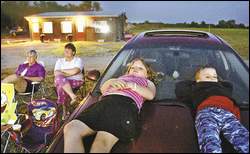 Katie Replogle, 9, from Ottumwa, and her brother Jacob, 5, watch a movie with their grandmother, Judi Glosser, from Centerville, far left, and their mother, Marsha Linney, at Sunshine Mine Drive-In west of Centerville. The concession stand and projection